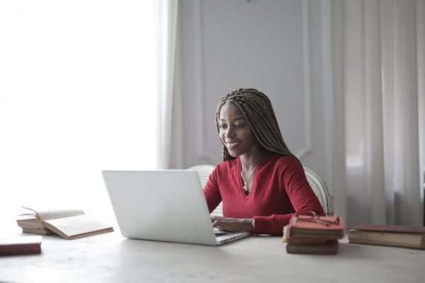 woman in red long sleeve shirt using macbook air Young black woman smiling and using laptop