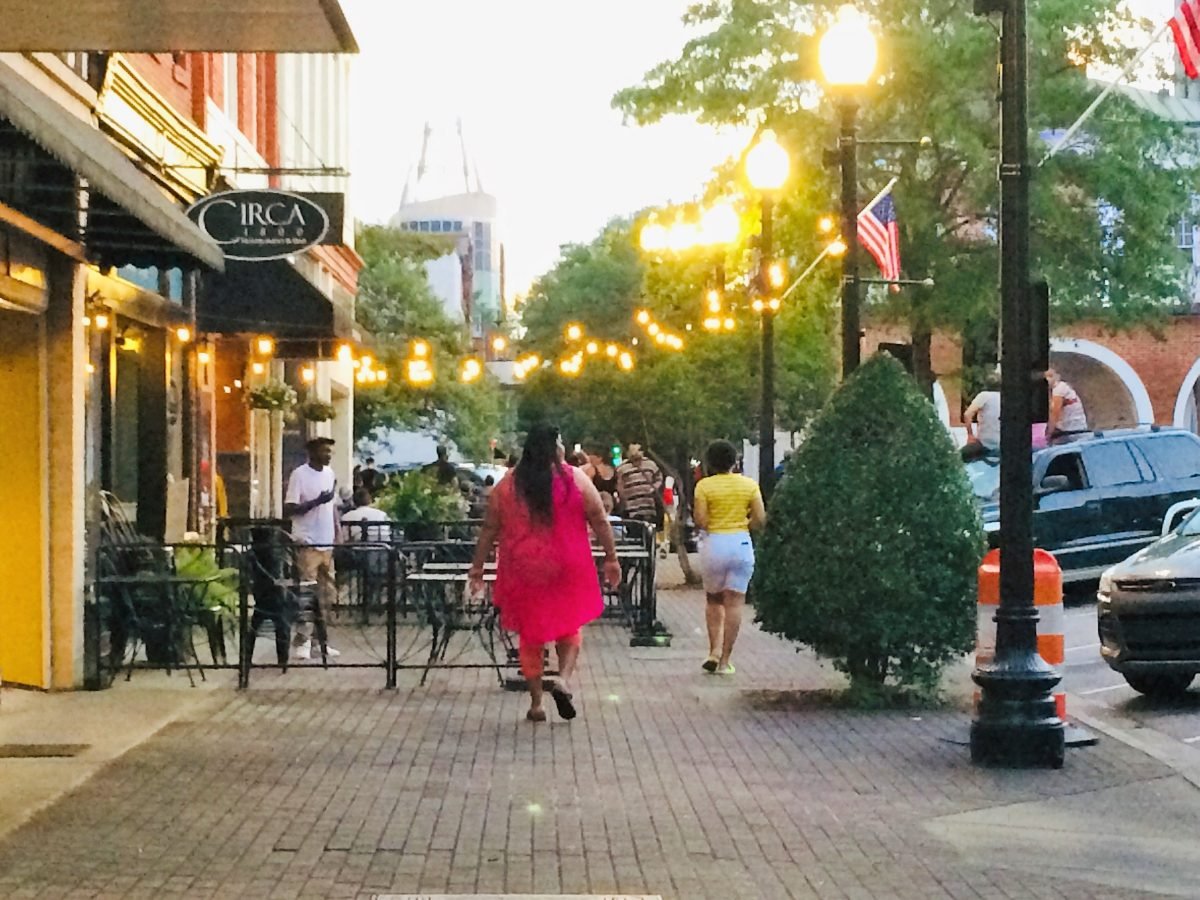 Things to do in Fayetteville, NC.: Scenery on Hay Street with people walking along the sidewalk while a string of lights hangs overhead near Circa 1800 restaurant.