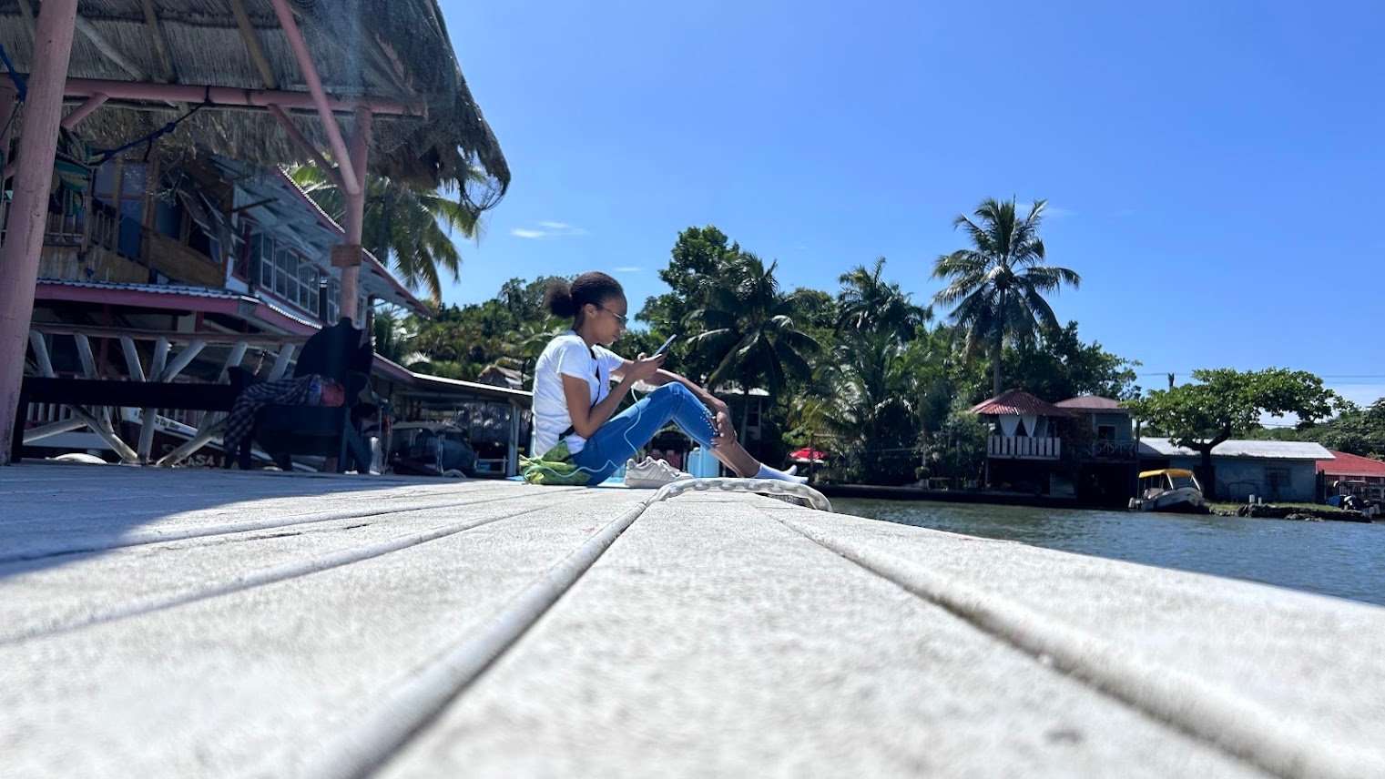 Curls Trip blogger sitting on pier looking at smartphone in Livingston, Guatemala